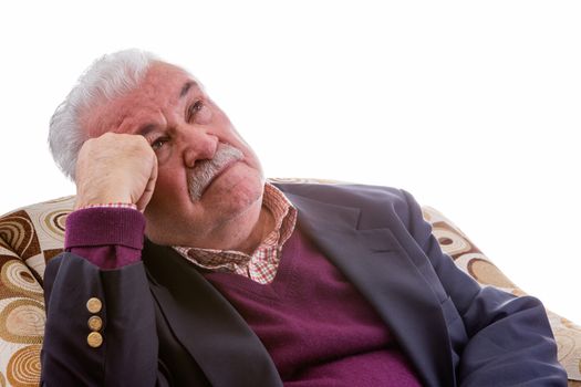 Elderly retired man relaxing in a comfortable armchair staring thoughtfully up into the air with an intent expression, isolated on white with copy space