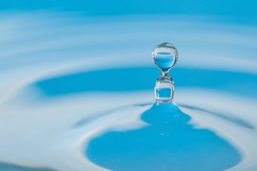 Droplet of water landing in a small dish lit by a blue flash