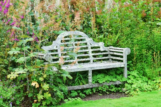 Beautifully designed old garden seat in pride of place in the summer sun, framed against the greenery of an English country garden.