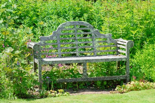 Beautifully designed old garden seat in pride of place in the summer sun, framed against the greenery of an English country garden.