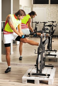 Young male with sport clothes is stretching in cycling gym.