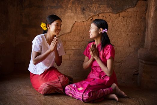 Two young Myanmar girl in a traditional welcoming gesture, sitting inside temple.