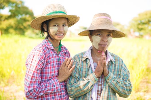 Portrait of a two Myanmar female farmers with thanaka powdered face showing greeting gesture at paddy field.