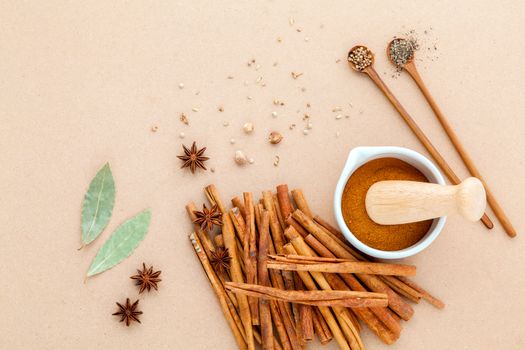 Composition of cinnamon stick and cinnamon powder in white mortar with star anise ,bay leaves and wooden spoon on brown background .