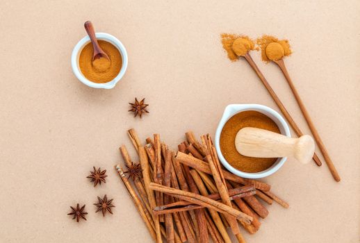 Composition of cinnamon stick and cinnamon powder in white mortar with star anise and wooden spoon on brown background .