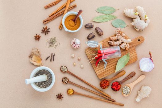 Composition of Mixed spices and herbs background cinnamon stick and cinnamon powder in white mortar with star anise ,bay leaves,onion ,ginger,galangal,saffron ,rosemary and wooden spoon on brown background .