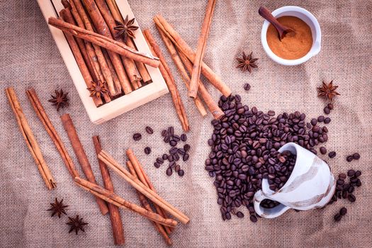 The Cup of coffee beans on the cloth sack with cinnamon sticks ,cinnamon powder in the bowl and star anise.