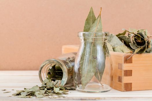 Bottle of dried bay leaves and wooden box with selective focus on wooden background.