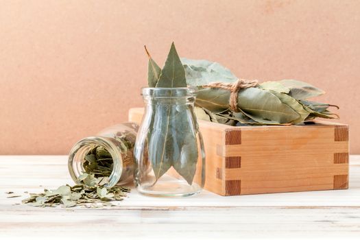 Bottle of dried bay leaves and wooden box with selective focus on wooden background.