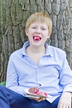 Boy sitting near tree and eating dessert with appetite