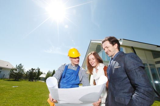 Worker shows house design plans to a young couple outdoors