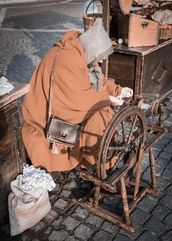 Elderly woman uses the cocoons of silkworms to spin using an old spinning wheel of wood.