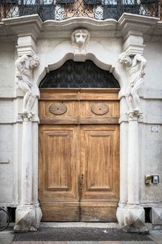 Old white stone entrance and wooden portal with statues that support the side columns.