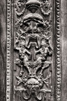 Detail of old wooden gate engraved with demonic figures.