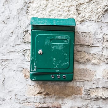 Old and shabby green mailbox attached to a stone wall.