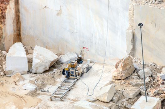 Industrial marble quarry, with cut blocks and workers and machines bulldozer at work.