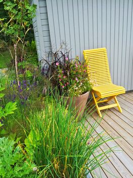 Summer patio decorated with flowers and yellow chair. House exterior.