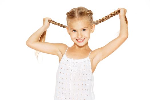 Funny little girl with a charming smile in a white dress holding a pigtails