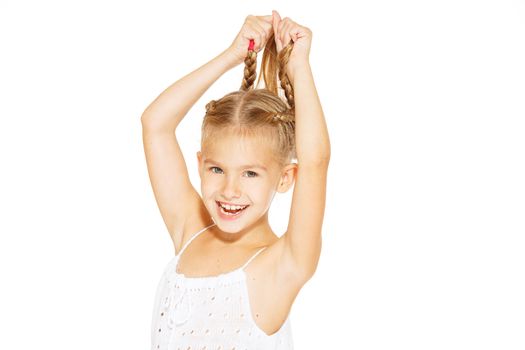 Funny little girl with a charming smile in a white dress holding a pigtails