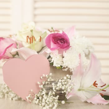 Beautiful bouquet of flowers in basket and heart shaped valentines day card on wooden background