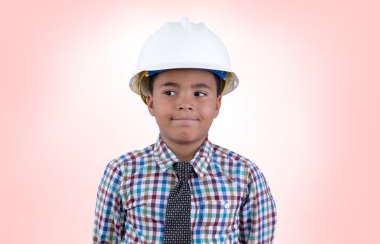 Playful little boy in white hard hat and necktie looking over over pink background