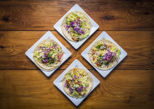 4 plated tacos shot on wood table from above