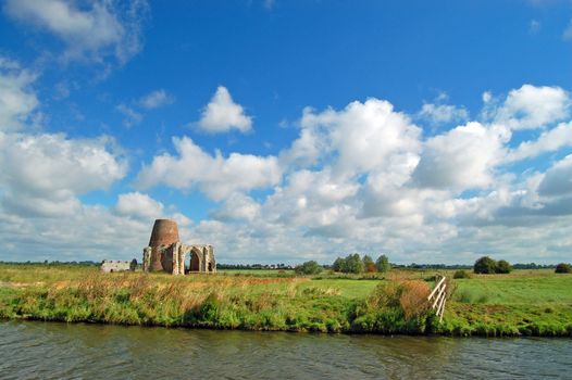A tranquil flat summer landscape, big skys and wide horizons, and a ruined windmill and church by the waterway ~ A typical view of the Norfolk Broads national park, in Norfolk, England. 