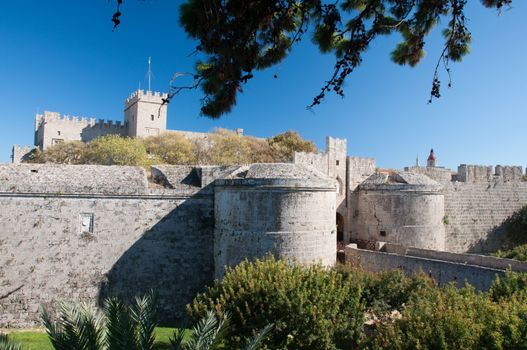 City walls and dry moat with the Palace of the Grand masters on the horizon, viewed from Dimokratias to Old  Saint Georges Gate, Rhodes Tow, Rhodes Island, Greece