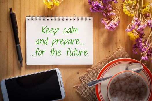 "Keep calm and prepare for the future" is written on notepad with pen, smart phone, and a cup of hot coffee on wood table in afternoon time