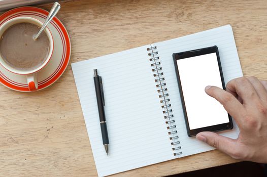 Male right hand using smart phone on wood bar beside window with notebook and coffee cup in cafe in morning time
