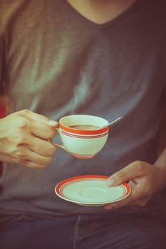 The man wearing grey t-shirt holding coffee cup in his hand in afternoon time with film filter effect