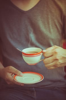The man wearing grey t-shirt holding coffee cup in his hand in afternoon time with film filter effect