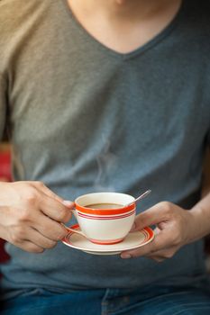 The man wearing grey t-shirt holding coffee cup in his hand in afternoon time