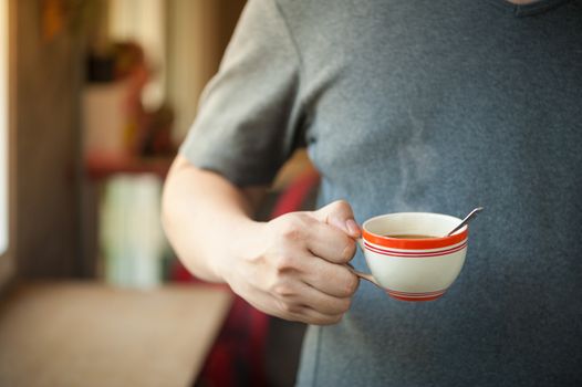 The man wearing grey t-shirt holding coffee cup in his right hand in afternoon time