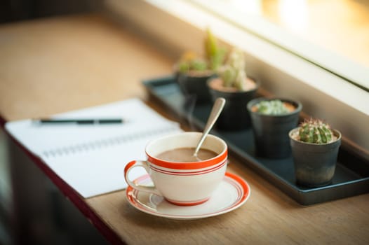 Coffee cup and opened notebook with pen on wood bar beside window at coffee shop in morning time