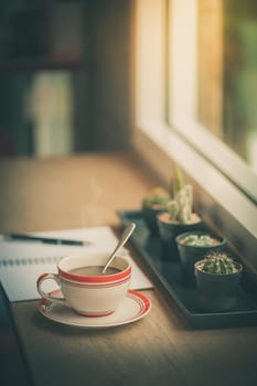 Coffee cup and opened notebook with pen on wood bar beside window at coffee shop in morning time with vintage filter effect
