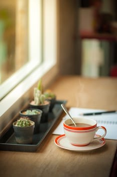 Coffee cup and opened notebook with pen on wood bar beside window at coffee shop in morning time