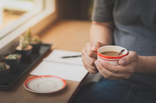 The man wearing grey t-shirt sitting beside window in cafe holding coffee cup in his hand in afternoon time with vintage filter effect