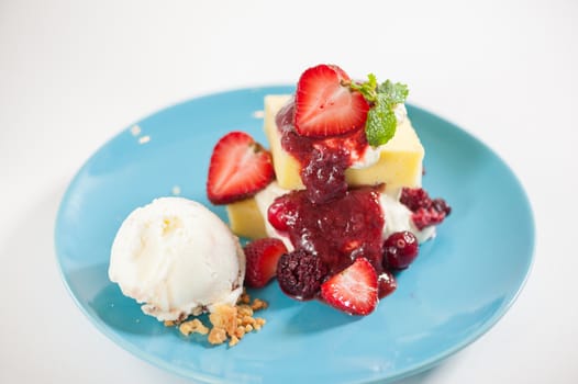 Yellow cake and vanilla ice cream dressed with strawberry sauce on blue dish