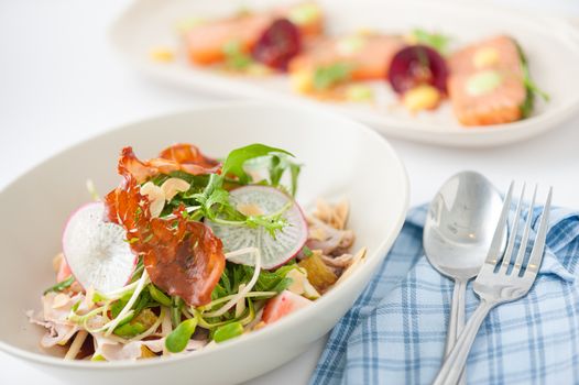 Vegetables and fruits salad with balsamic vinegar and navel orange dressing and smoked striploin ham 1.5 millimeters thickness in ceramic bowl, a modern cusine concept food with another dish of appetizer in background