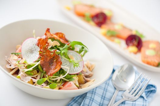 Vegetables and fruits salad with balsamic vinegar and navel orange dressing and smoked striploin ham 1.5 millimeters thickness in ceramic bowl, a modern cusine concept food with another dish of appetizer in background