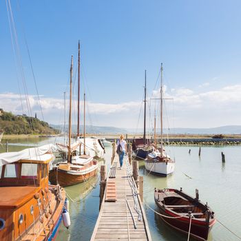 Woman strolls along wooden pier between traditional fishing boats at old fishing port in Secovlje, Slovenia. Summertime feeling. Landscape format.