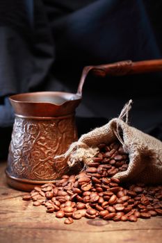 Jute sack with coffee beans near vintage copper pot