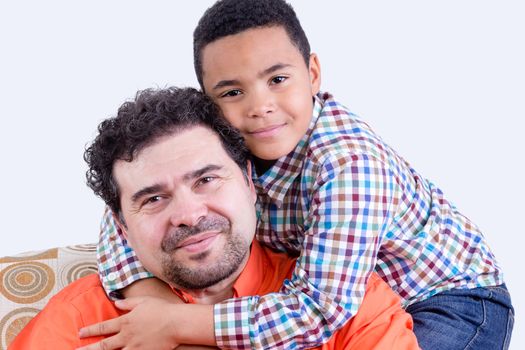 Cheerful child in checkered shirt with grin hugging his smiling father with beard from behind