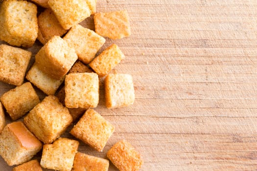 Crispy golden freshly sauteed croutons made of cubed white bread as a delicious crunchy addition to a bowl of hot winter soup, overhead on wood with copy space