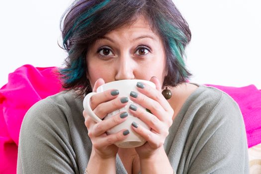 Excited woman with wide eyes and painted fingernails holding coffee mug partially covering her face