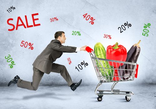 Businessman with vegetables in shopping cart on grey background