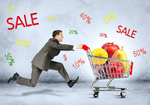 Businessman with fruits in shopping cart on grey background