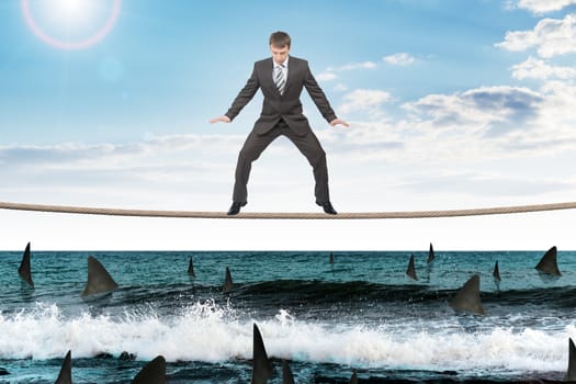 Businessman standing on rope above ocean with sharks