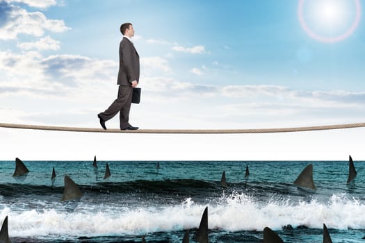 Businessman walking on rope above ocean with sharks